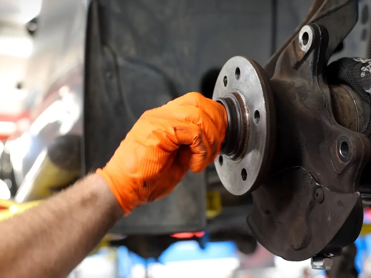 Mechanic in gloves working on a wheel hub under a vehicle